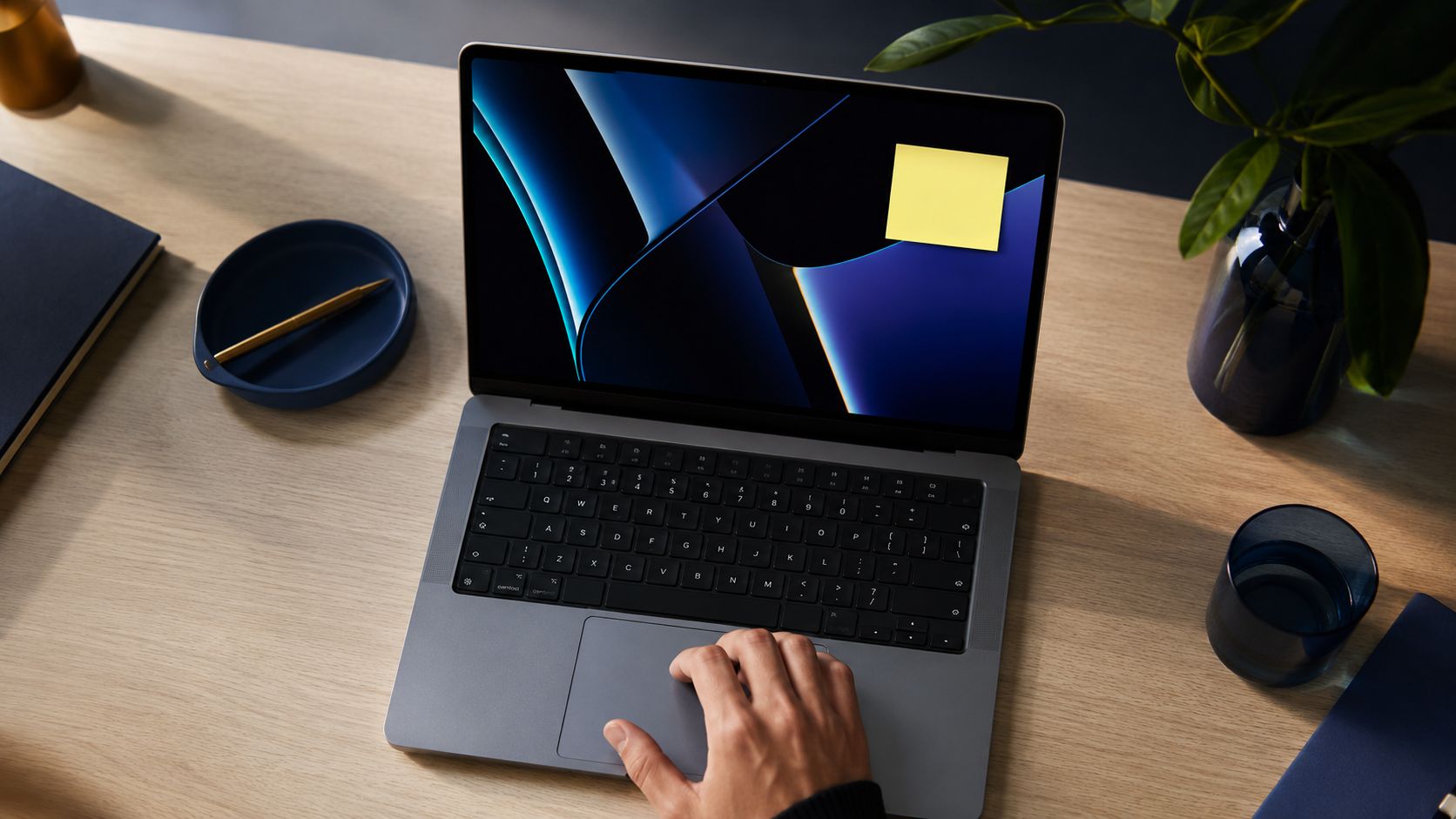 Una mano usa il trackpad di un computer portatile con un post-it giallo sullo schermo su una scrivania